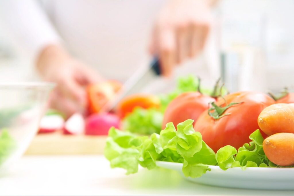 A person cutting tomatoes on top of lettuce.