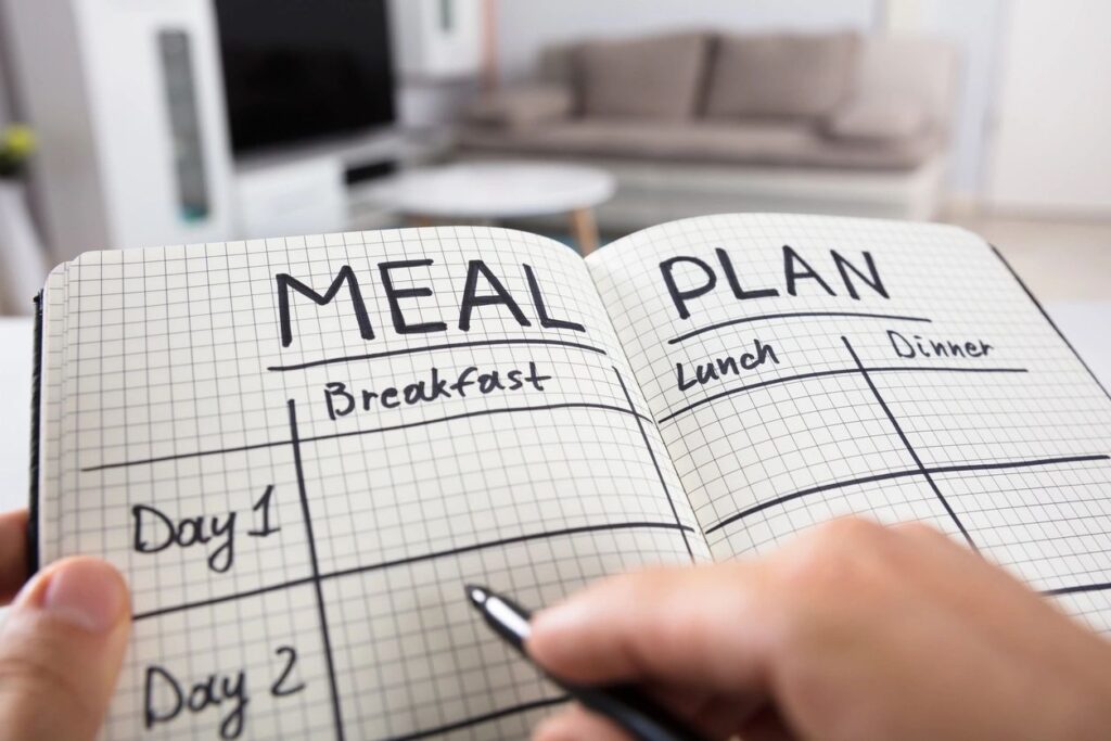 A person writing on the pages of a meal plan book.